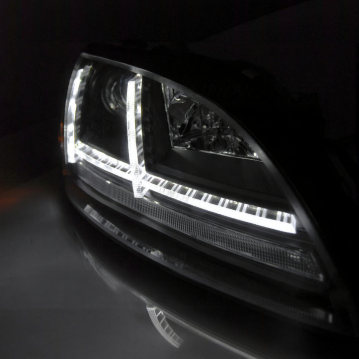 Nahaufnahme eines schwarzen LED-Auto-Scheinwerfers bei Nacht mit hellem, L-förmigem Lichtstreifen.