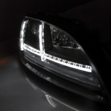 Nahaufnahme eines schwarzen LED-Auto-Scheinwerfers bei Nacht mit hellem, L-förmigem Lichtstreifen.